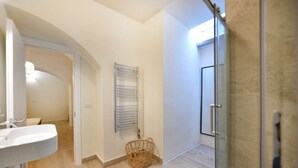 Ein Badezimmer mit einem weißen Waschbecken, einer Glasdusche und einem Korbwannenstuhl.