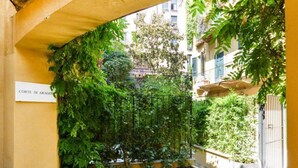 Ein Innenhof mit einer Pergola, die mit Grün bewachsen ist, einem verschlossenen Eingang und einem Gebäude mit Balkonen.