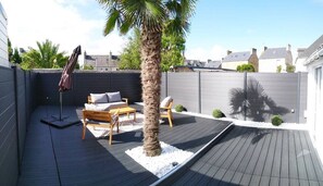 Um terraço com uma palmeira, um banco de madeira e uma mesa com cadeiras.
