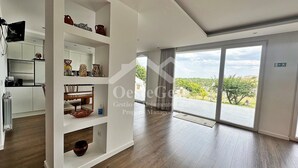 En rummelig opholdsstue med en stor skydedør, der fører ud til en balkon med udsigt over grønne områder.