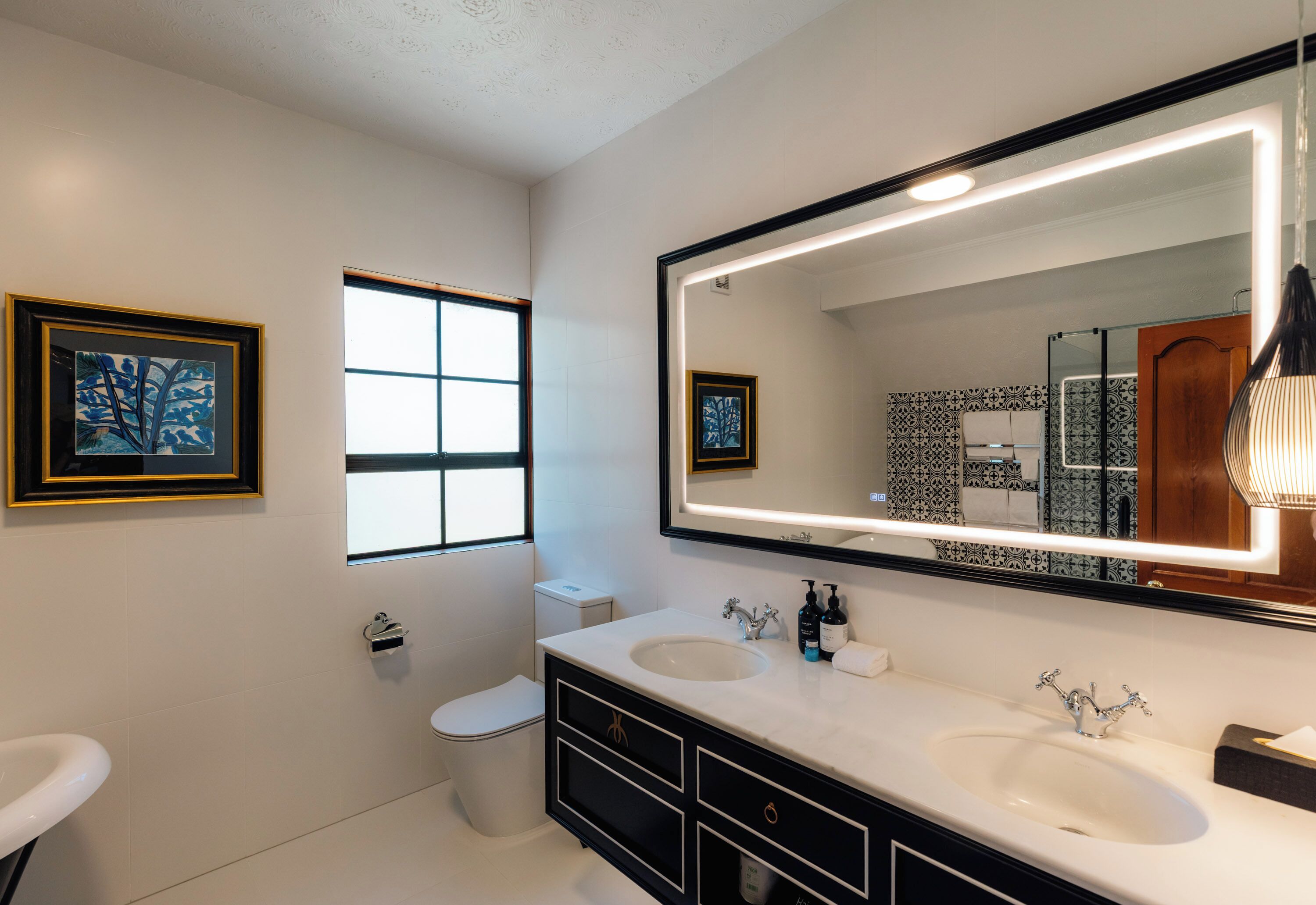 Un baño moderno con dos lavamanos, un espejo grande y un inodoro.