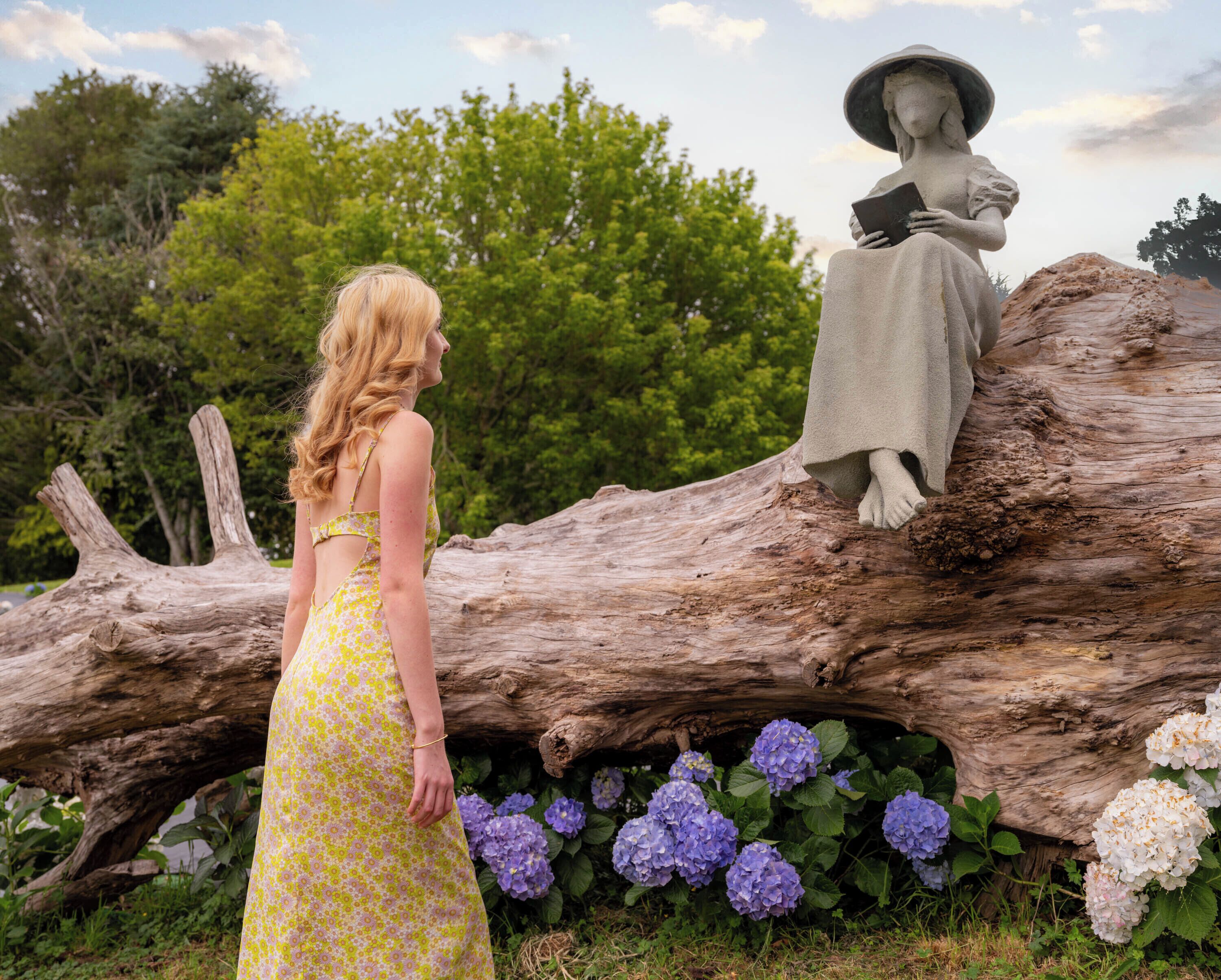 A statue of a woman reading a book, a large log, and purple hydrangea flowers.