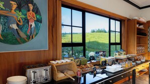 A breakfast buffet with a view of a green field through large windows. - Hana Lodge (Rotorua)
