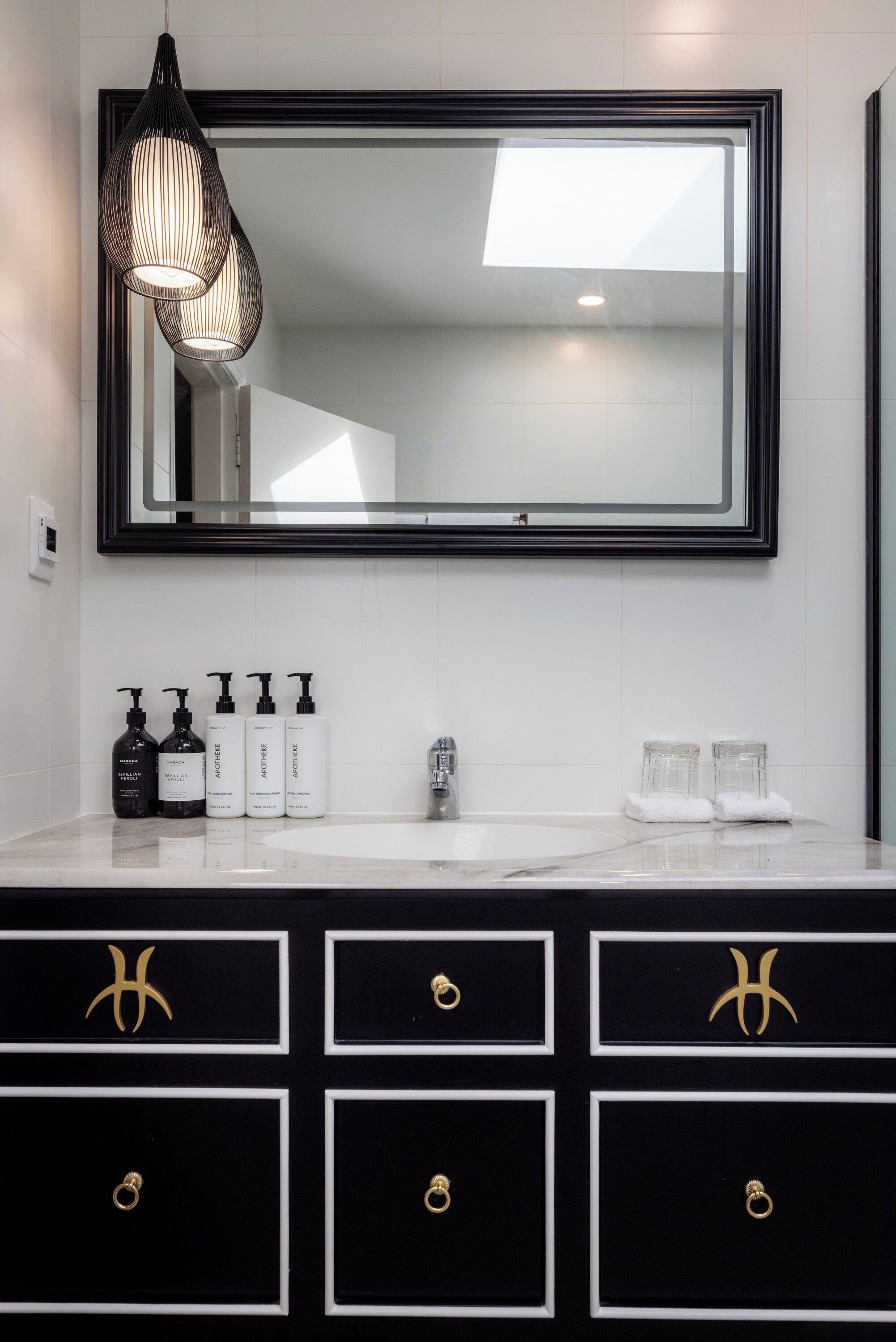 Une salle de bain dotée d’un grand miroir, d’un meuble-lavabo noir et blanc et de produits de toilette.