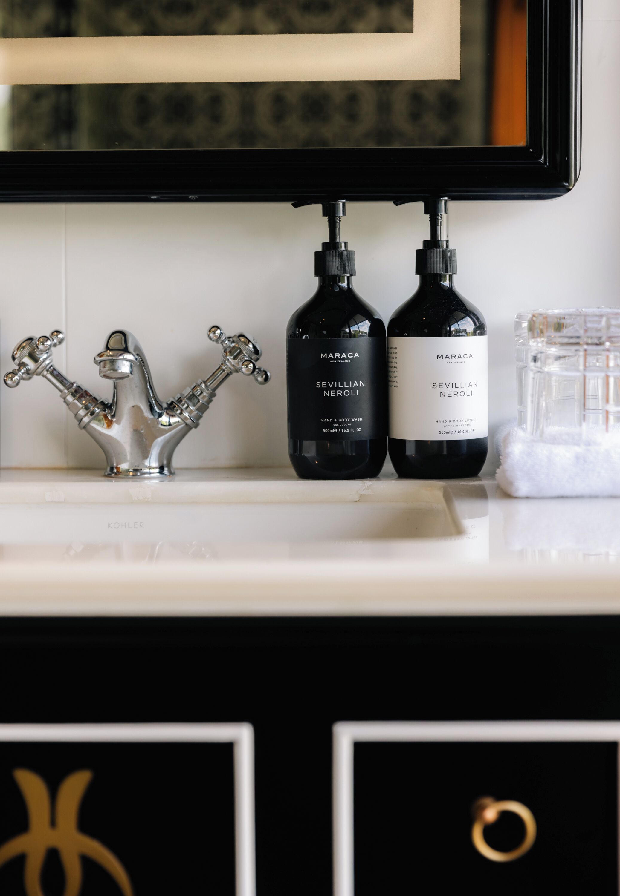 A bathroom vanity with a chrome faucet, two bottles of Maraca Sevillian Neroli hand and body wash, and a clear soap dispenser.