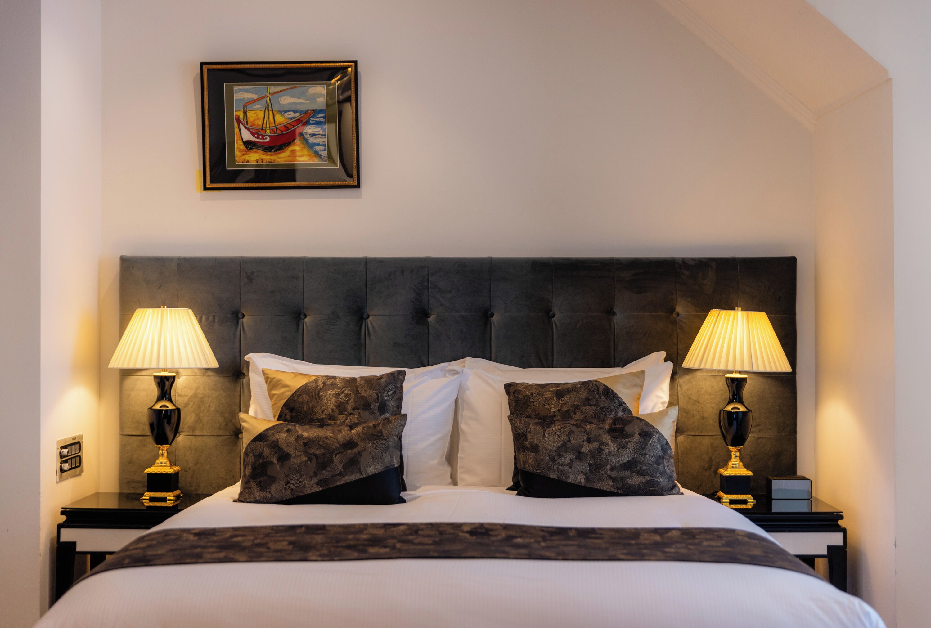 Een net opgemaakt bed met een gestuufd hoofdbord, twee bedlampjes en een ingelijst foto op de muur.