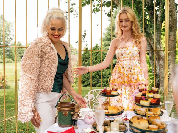 Two people at an outdoor event with a table of food and drinks.