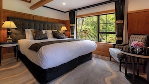 Una cama grande con cabecera, dos mesitas de noche con lámparas, una silla y una ventana con vistas a zonas verdes.