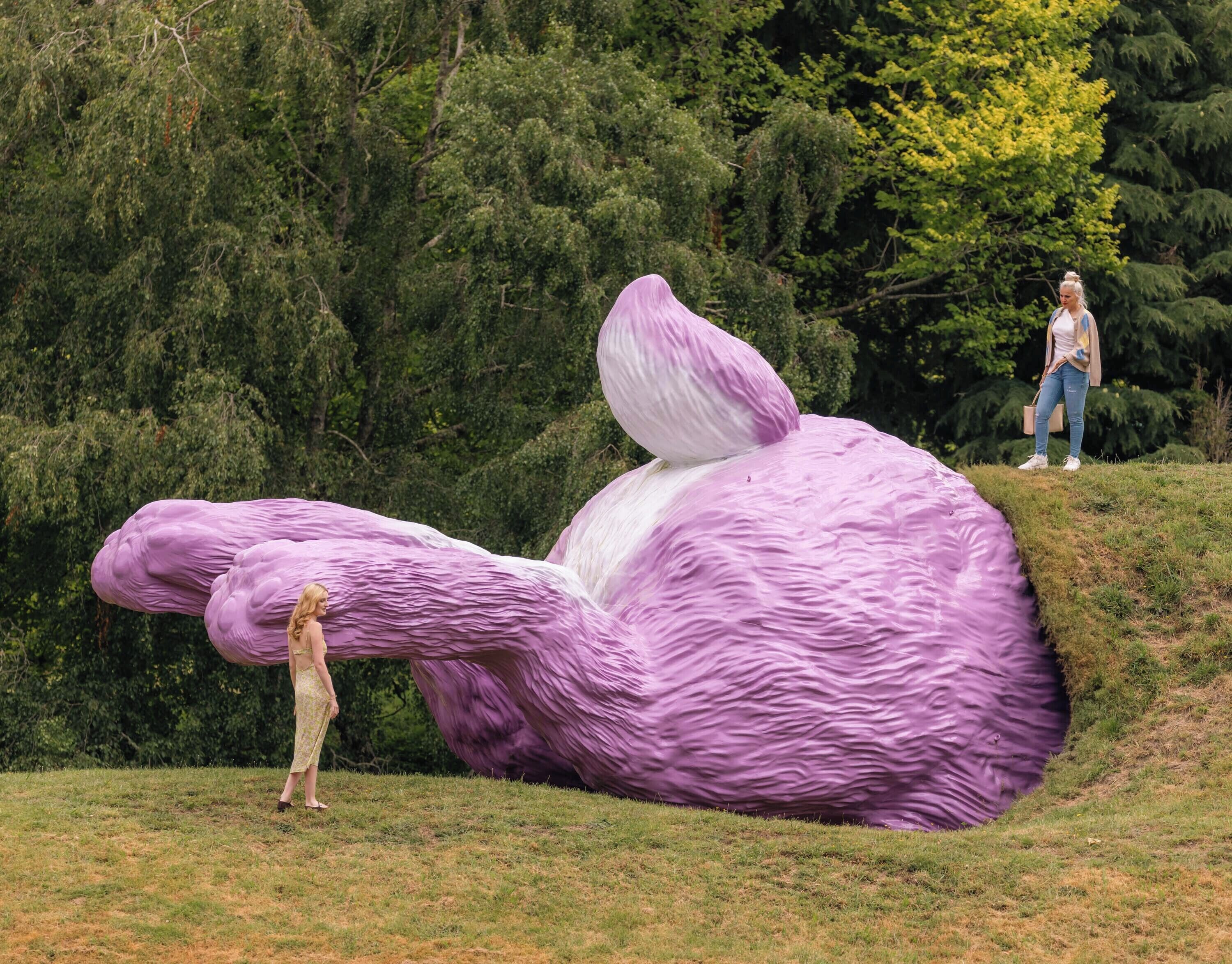 A large purple sculpture of a creature in a grassy field with dense trees in the background.
