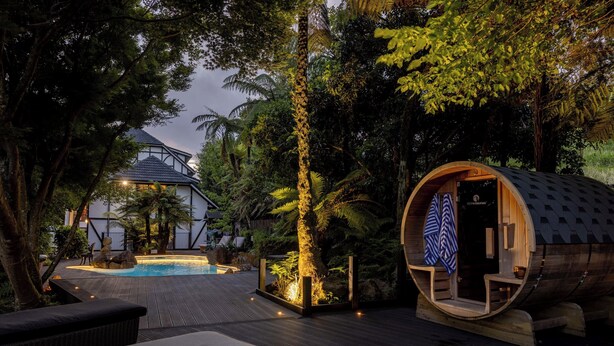 Una estructura de madera con un banco y una pequeña piscina en un jardín exuberante.