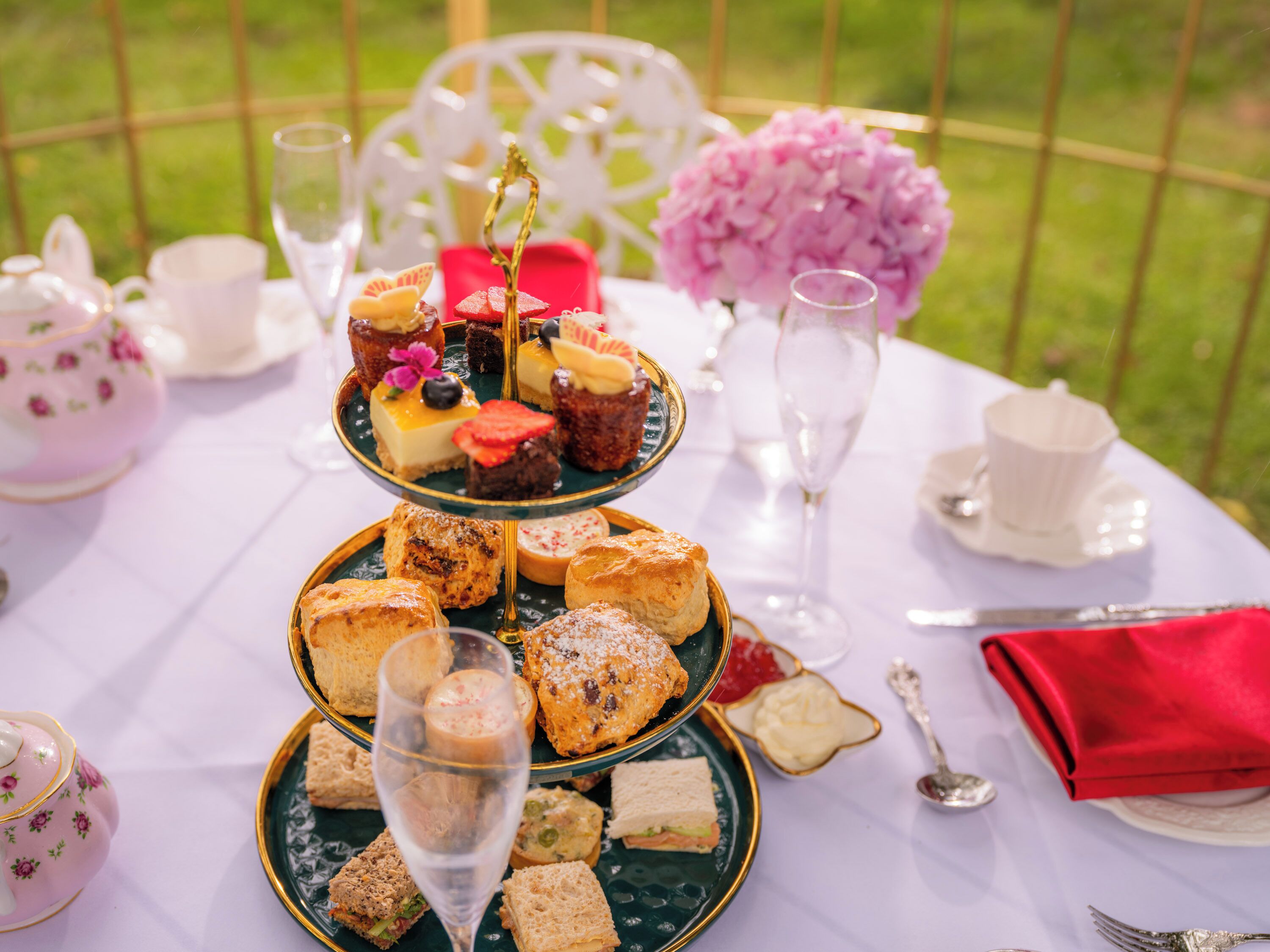 A three-tiered dessert stand with various pastries and a glass of champagne on a white tablecloth.