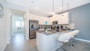 Una cocina moderna con gabinetes blancos, electrodomésticos de acero inoxidable y una isla central con taburetes de bar.