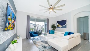Una sala de estar moderna con un sofá blanco, sillones azules, una mesa de centro y un ventilador de techo.