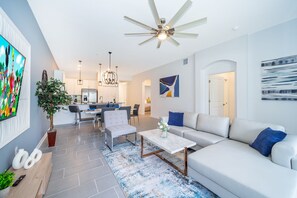 Un salon moderne avec un canapé blanc, une table basse et un coin repas agrémenté d’un lustre.