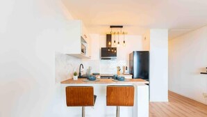 Una cuina moderna amb una illa central, dos tamborets d'esbarjo, un refrigerador negre i il·luminació penjant.