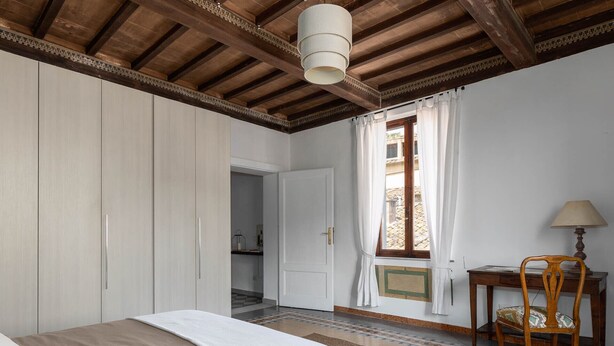 Une chambre à coucher avec un lit, un bureau avec une chaise, une fenêtre avec des rideaux et un plafond en bois.