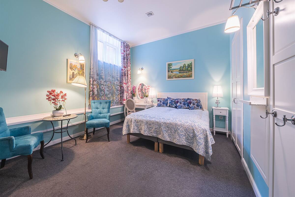 Une chambre à coucher avec un lit, deux chaises, une petite table avec une lampe et une table de chevet avec une lampe.
