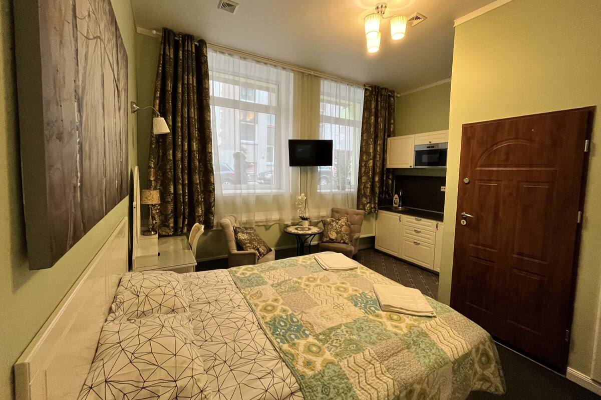 Une chambre d’hôtel équipée d’un lit, d’un bureau, d’une chaise, d’une télévision, d’une kitchenette et d’une porte.
