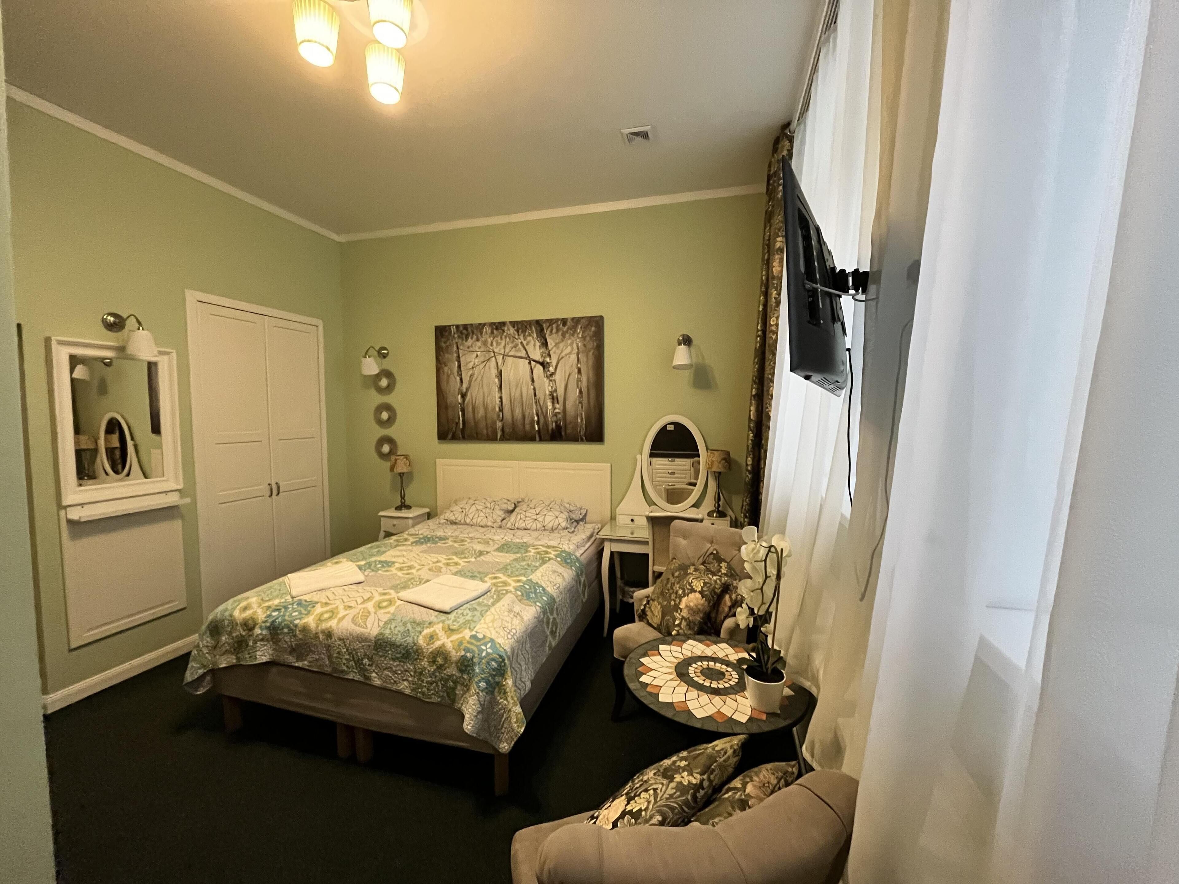 A bedroom with a bed, bedside table, chair, and a painting on the wall.