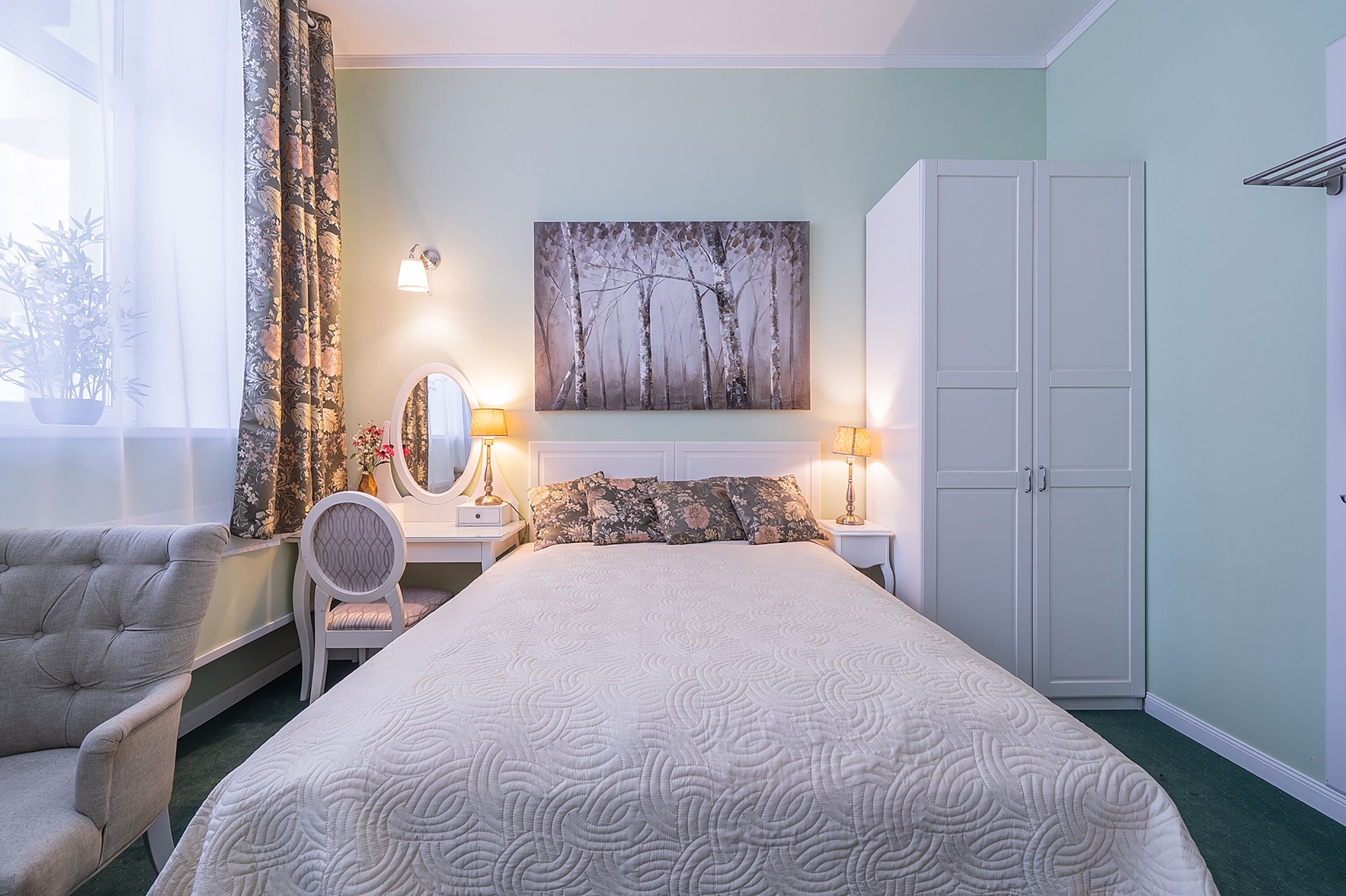 A bedroom with a bed, a chair, a dresser, a mirror, and a painting on the wall.
