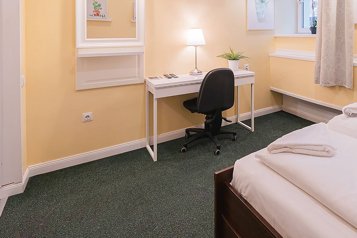 Une chambre d’hôtel avec un lit, un bureau, une chaise, une lampe et une fenêtre avec des rideaux.