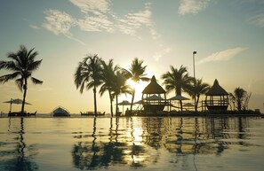 A resort pool area with palm trees and a gazebo structure during sunset.