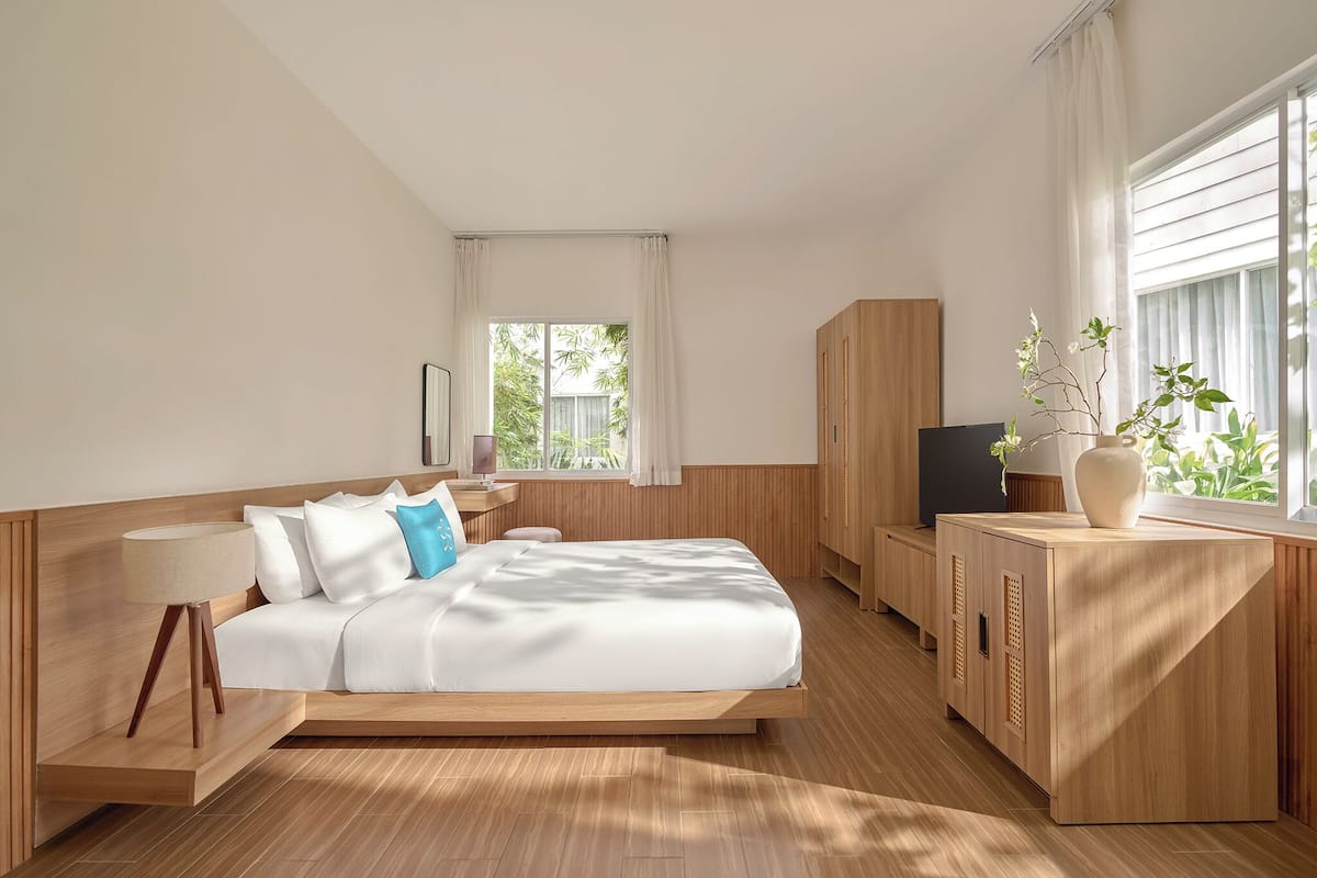 Una habitación de hotel moderna con una cama de madera, televisión, escritorio y ventana con cortinas.