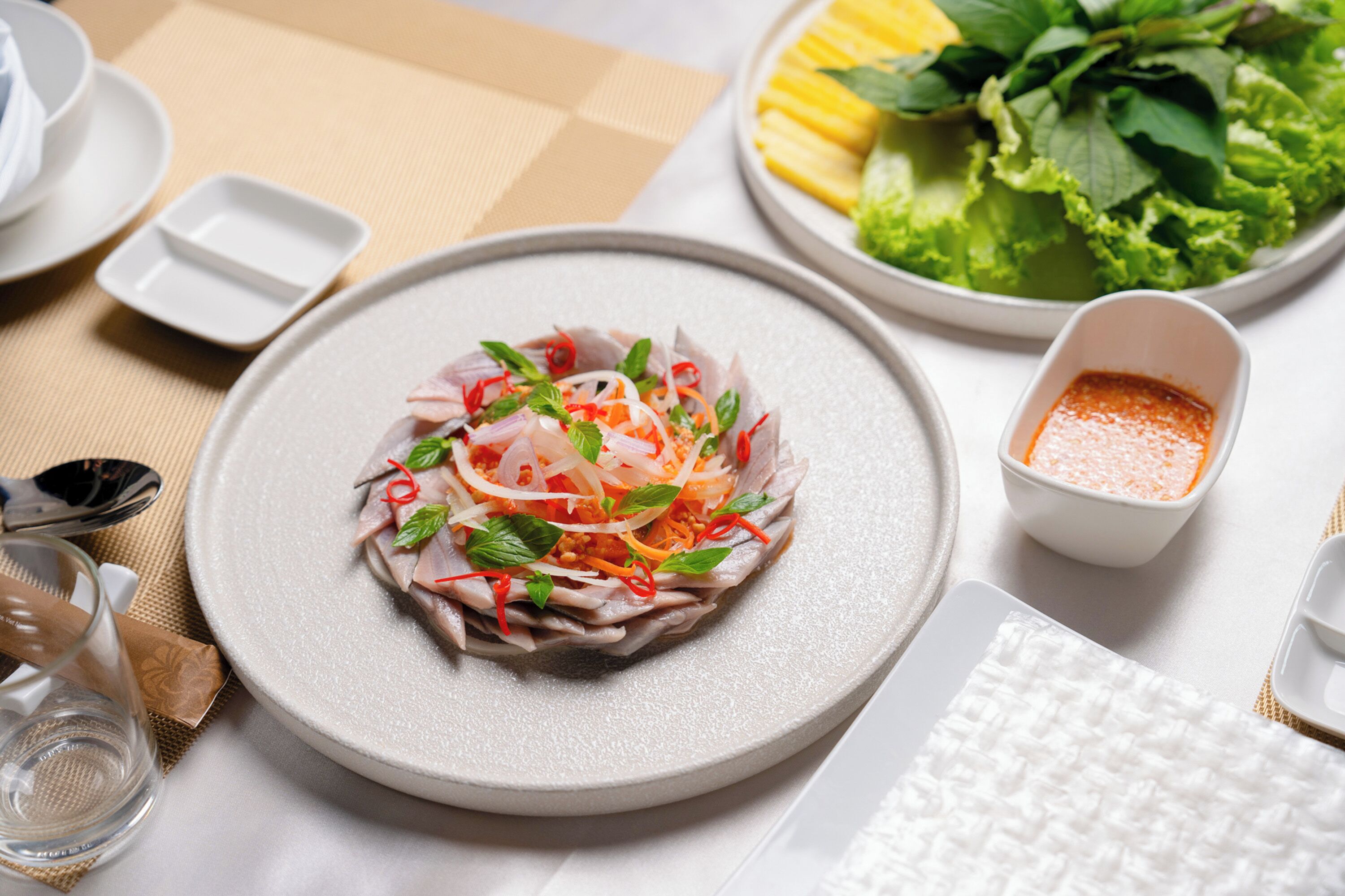 Una ensalada fresca con diversos vegetales y hierbas, acompañada de una porción de salsa y un plato de verduras verdes.