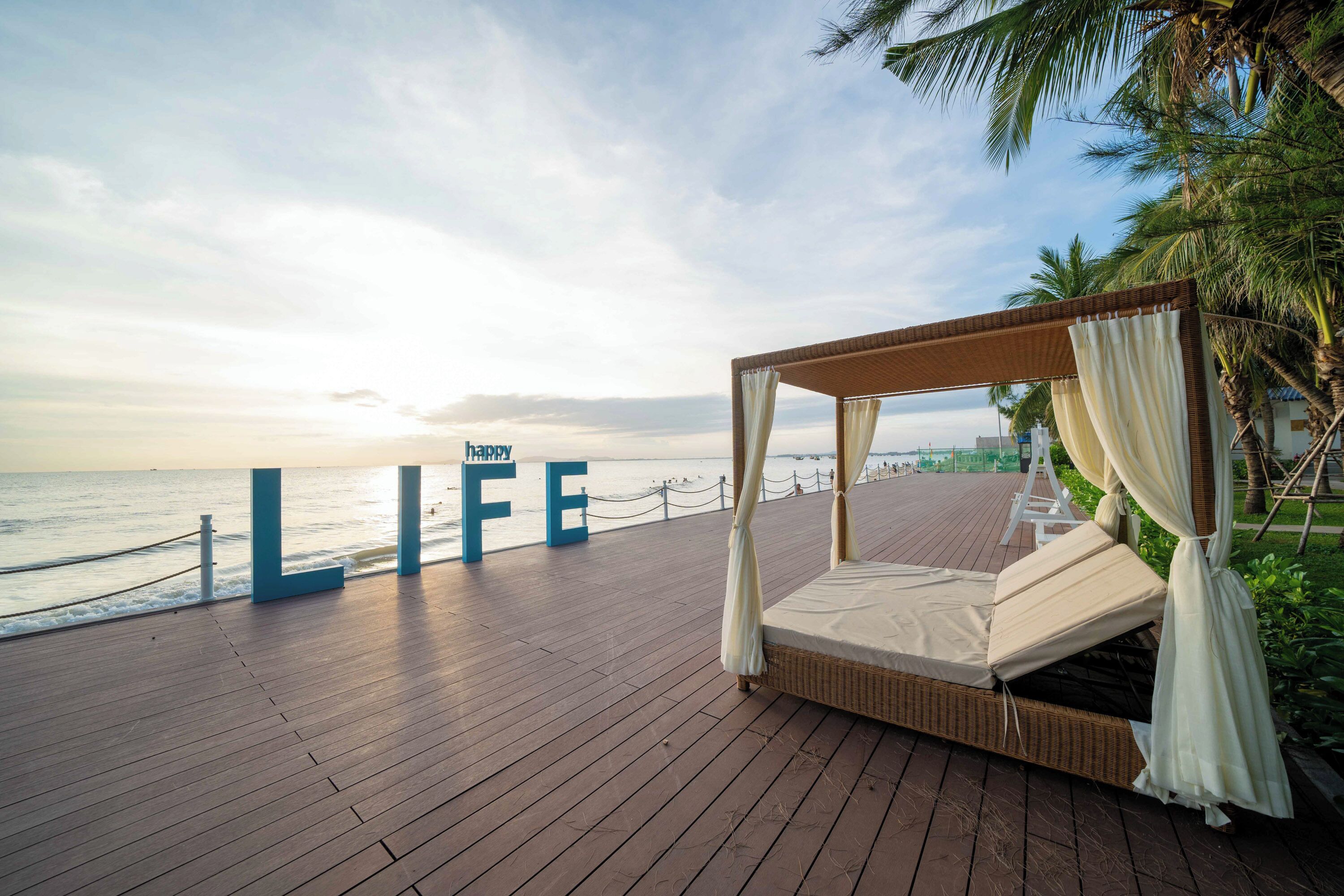 A wooden deck with a four-poster bed, a view of the sea, and the words "LIFE" and "BEAUTY" in the background.