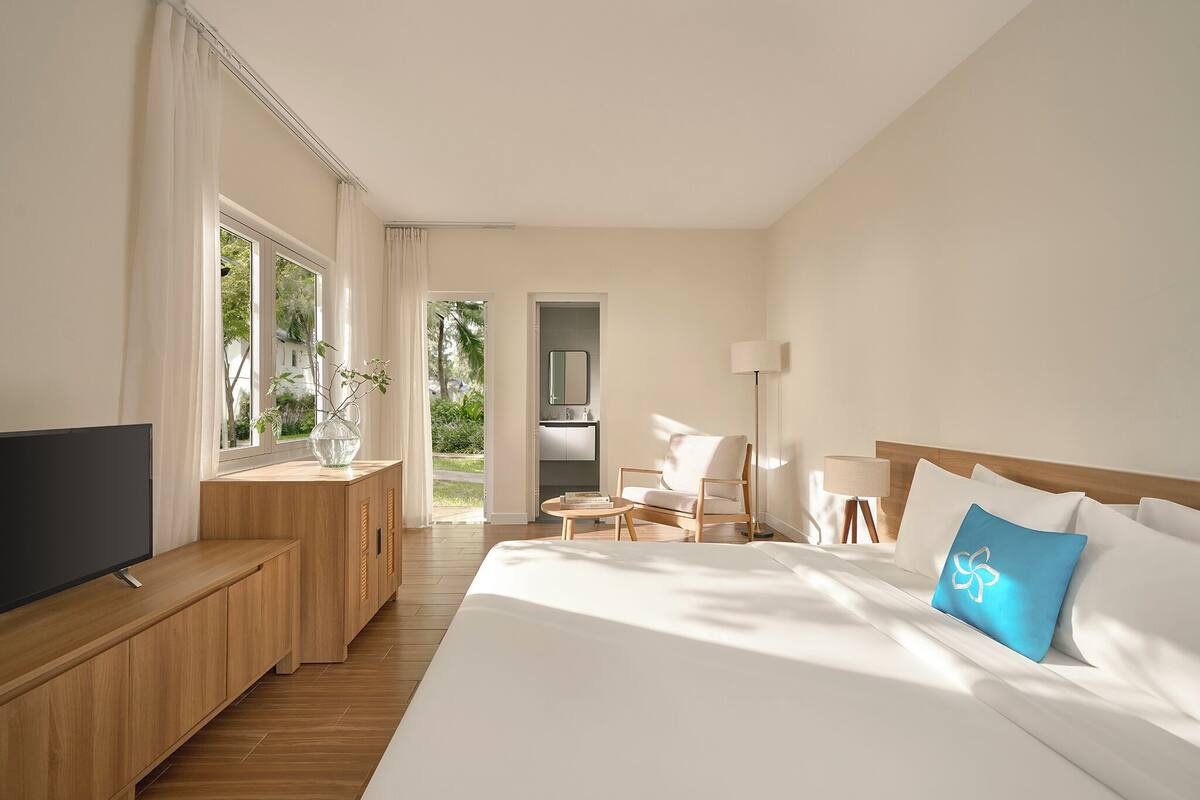 Habitación de hotel con una cama grande, un televisor sobre una consola de madera, un escritorio con una lámpara y vistas al exterior.