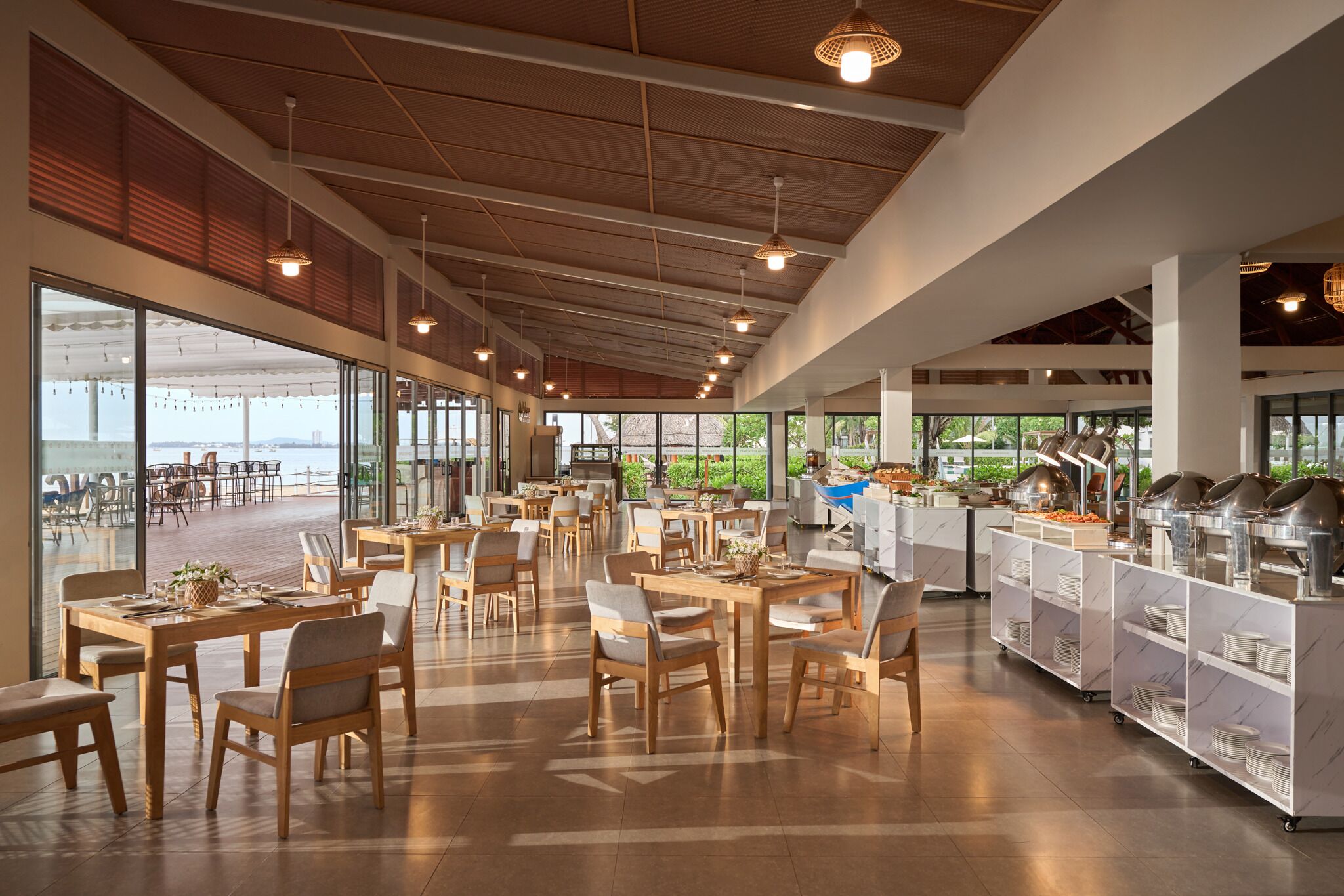 Un comedor amplio con mesas y sillas de madera, ventanas grandes que ofrecen vistas al exterior y una estación de bufé con diversas opciones de comida.
