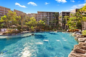 Une piscine de villégiature entourée de palmiers et un immeuble à plusieurs étages doté de balcons.