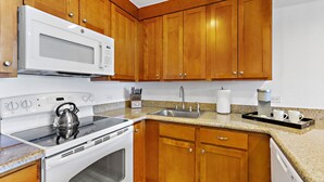 A kitchen with wooden cabinets, a white microwave, a stove, a sink, and a coffee maker. - Tropical charm, ocean touches - A guest favorite (Lahaina)