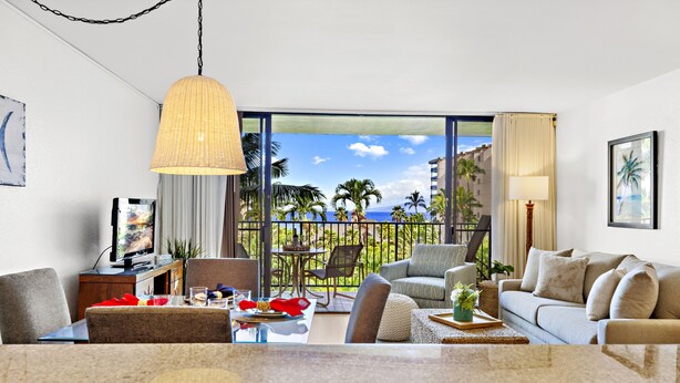 A modern living room with a large window, a dining area, and a sofa. - Tropical charm, ocean touches - A guest favorite (Lahaina)