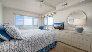 A bedroom with a bed, a ceiling fan, a TV, a dresser, and a window with a view of the ocean. - Direct oceanfront two bedroom condo ideally located on 77th street in Ocean City (Ocean City)