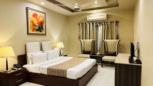 Una habitación de hotel con una cama grande, dos mesitas de noche, un escritorio, una silla, un aire acondicionado y un ventilador de techo.