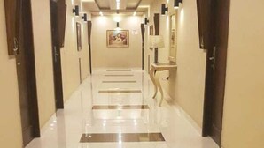 Un pasillo de hotel con piso de baldosas brillantes, puertas de madera y luces fijadas a la pared.