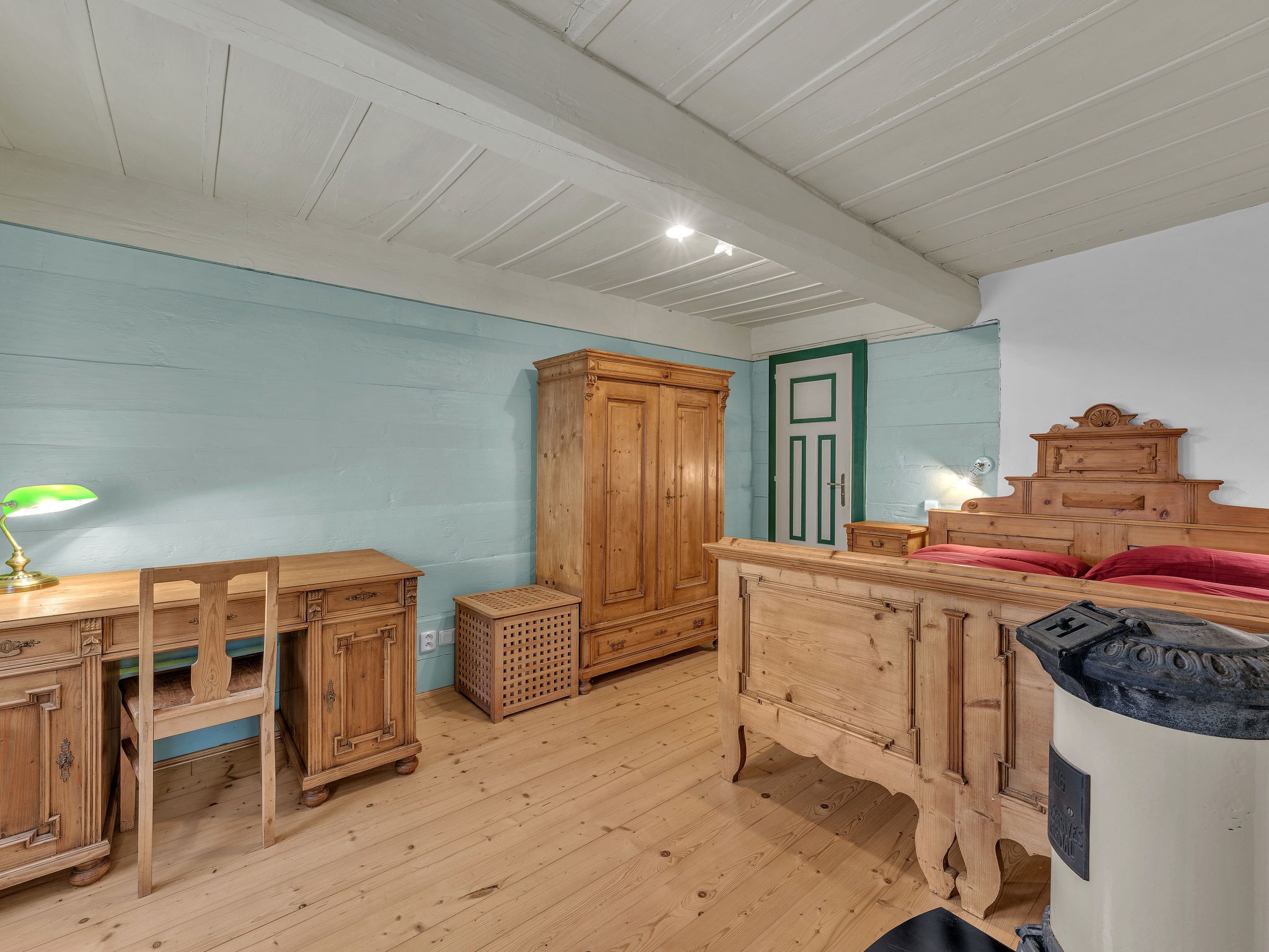 A room with wooden furniture, including a desk with a lamp, a wardrobe, and a bed with a headboard.