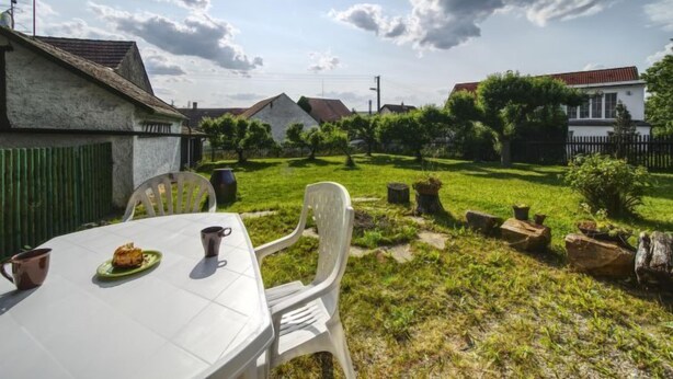 Une table blanche, entourée de chaises, avec une assiette de nourriture dessus, le tout installé dans un espace extérieur ensoleillé, avec une pelouse verdoyante et quelques arbres.