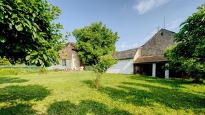 Une cour verdoyante avec un bâtiment blanc, un arbre et une clôture.