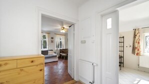 Un couloir mène à un salon où se trouvent un canapé, une table à manger et une chaise. Un buffet en bois et un radiateur sont fixés au mur.