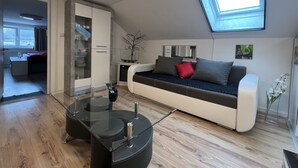 A modern living room with a glass coffee table, a sofa with cushions, a skylight, and a view of a kitchen area.