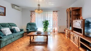 A living room with a green sofa, a wooden coffee table, a TV stand, and a large window with curtains. - Vacation home Reaa by Interhome (Barban)