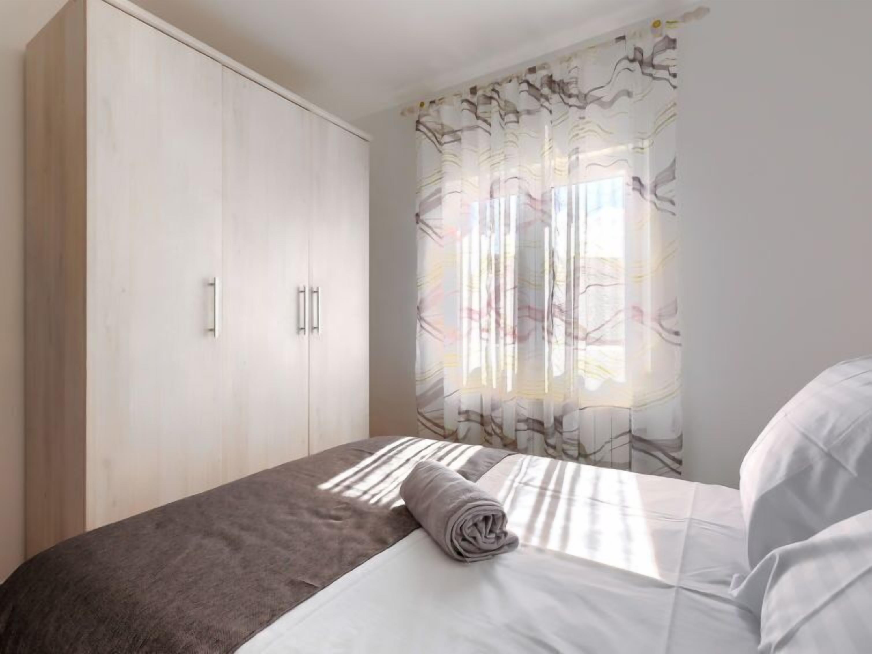 A bedroom with a bed, a wardrobe, and a window with floral curtains.