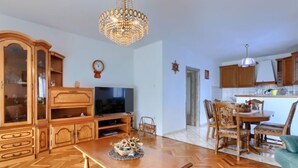 A spacious living room with a wooden herringbone floor, a dining area with a wooden table and chairs, a television, and a chandelier. - Vacation home Reaa by Interhome (Barban)