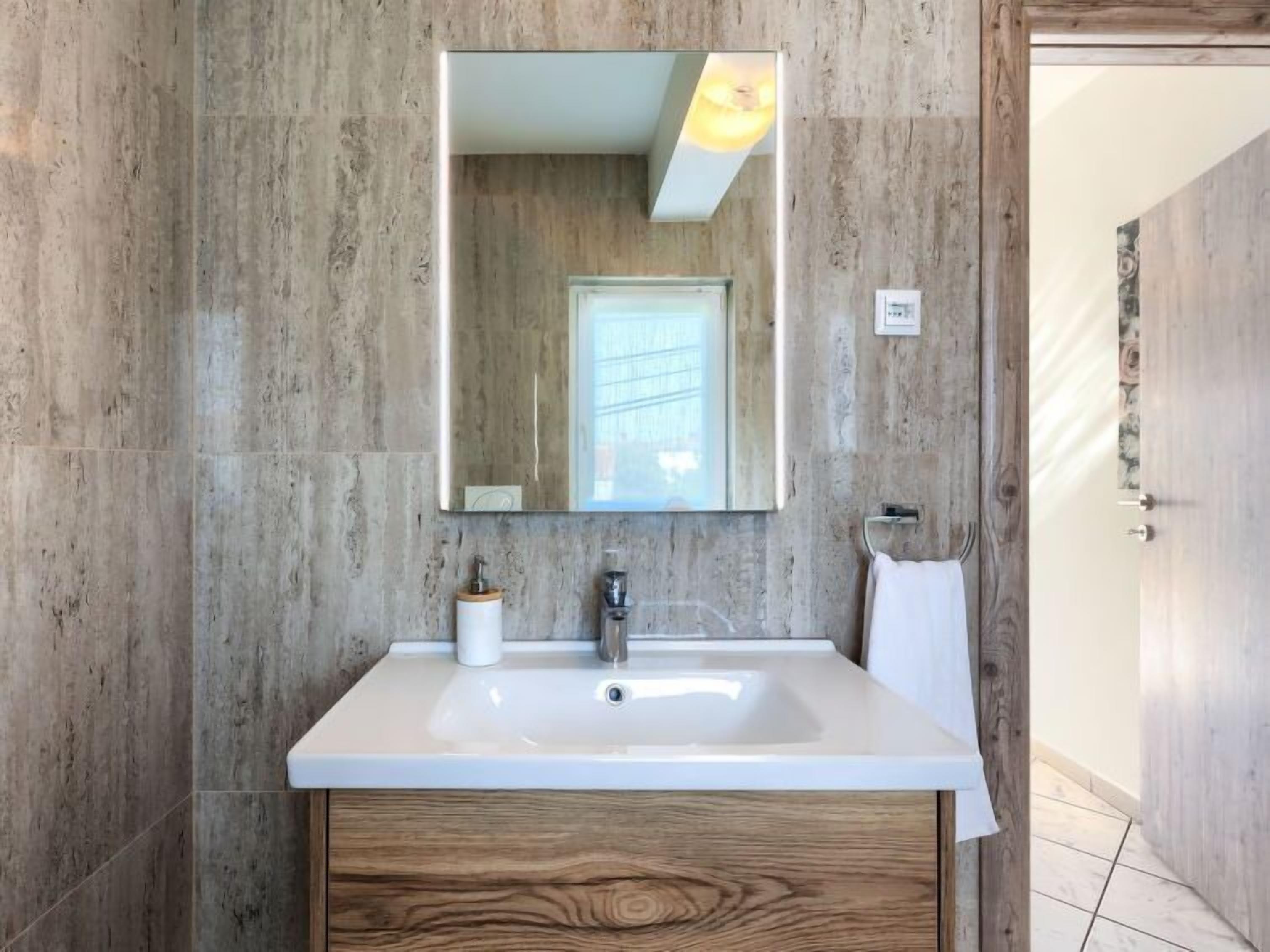 Un baño moderno con un espejo grande, lavamanos blanco y tocador de madera.