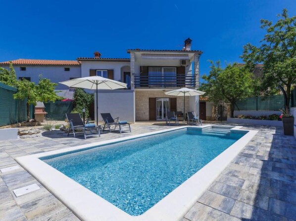 A rectangular swimming pool with lounge chairs and umbrellas, surrounded by a stone patio. - Vacation home Reaa by Interhome (Barban)