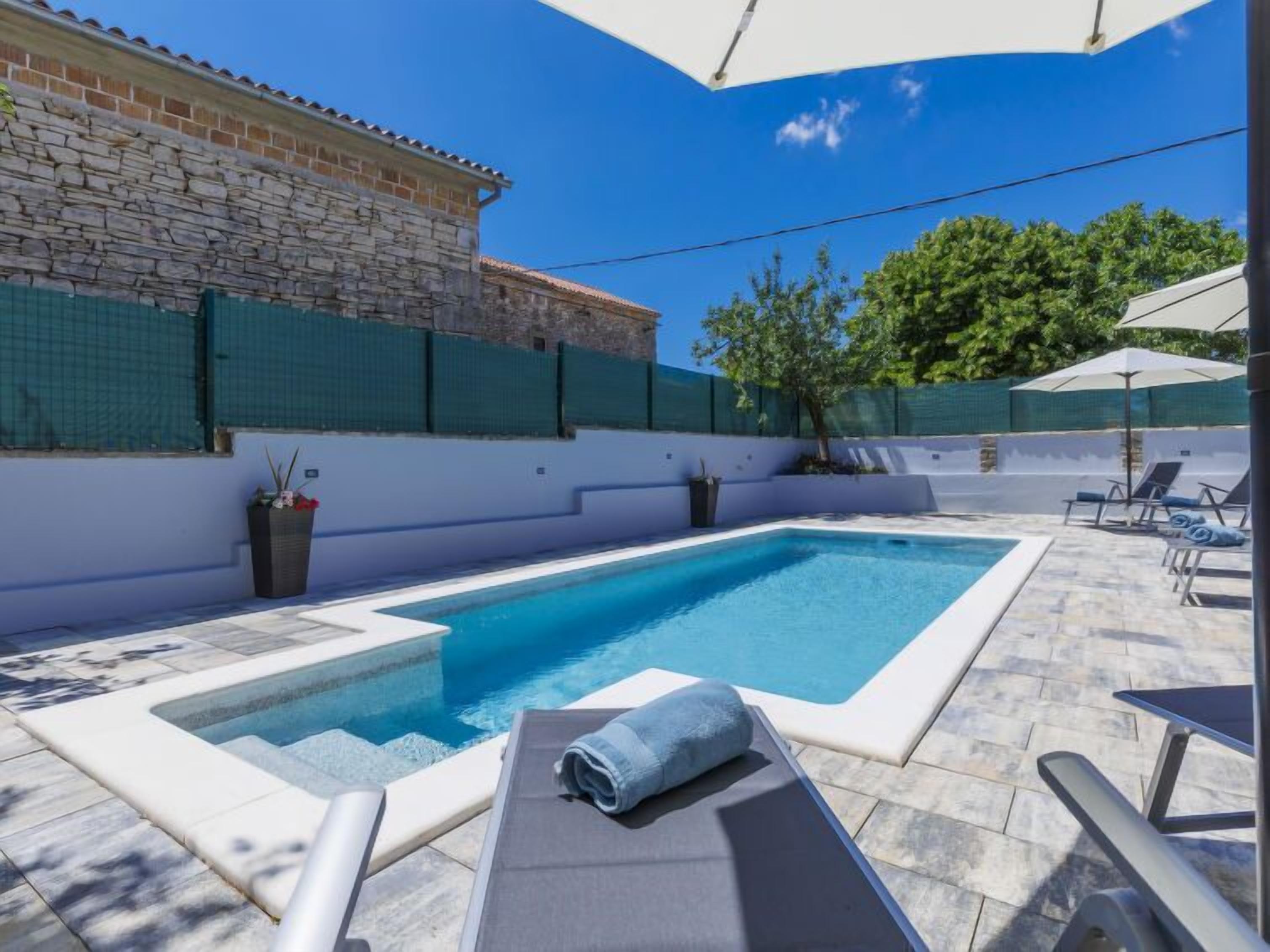 En swimmingpool med et lille spa, liggestole og en overdækket terrasse.