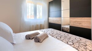 A modern bedroom with a bed, a large mirror, and a window with curtains. - Vacation home Reaa by Interhome (Barban)
