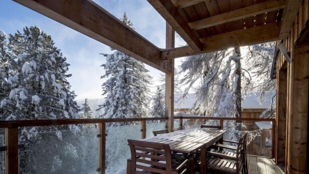 Une terrasse en bois avec une table et des chaises, d’où l’on peut admirer les arbres couverts de neige.